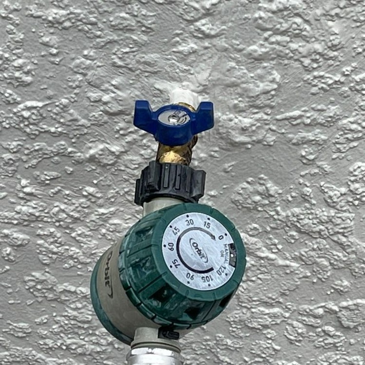 Repaired outdoor hose bib with a water timer on a stucco wall